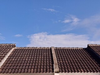 A clean view of brown clay roofing tiles against a bright sunny blue sky with light clouds, ideal for real estate, housing, and construction themes.