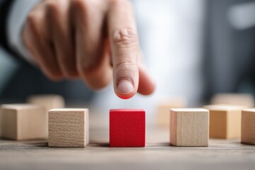 Finger points toward a single red wooden block among many beige ones.