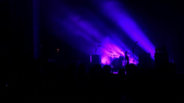 Purple lights and smoke from a fog machine from an empty stage at a rock music performance. Crowd audience waits in anticipation of a live band.