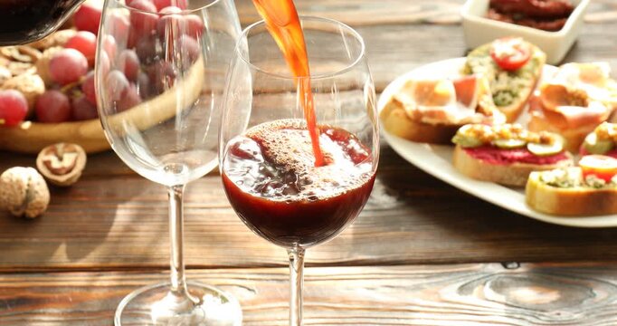 Pouring wine into glasses on wooden table with bruschette, grapes and nuts
