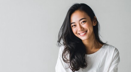 Young woman with dark hair smiling against a light gray background.