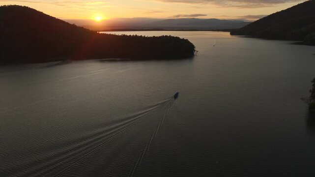 Aerial sunset over lake with boat leaving long wake