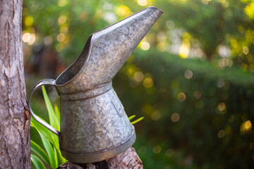 A vintage metal watering can hanging on a wooden fence in a garden