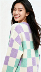 Woman wearing pastel checkered sweater smiles over her shoulder with long dark hair, offering a friendly and approachable portrait against a light neutral background with clear empty space available f