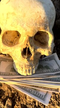 Skull With Money on Ground Symbolizes Greed, Mortality. Skull on ground with bundles cash dollars. Wealth, death, greed, human nature. Skeleton with money. Skull with dollar bills money. Dead.