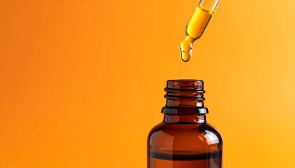 Glass dropper dispensing yellow essential oil or cosmetic serum into a brown bottle on an orange background.