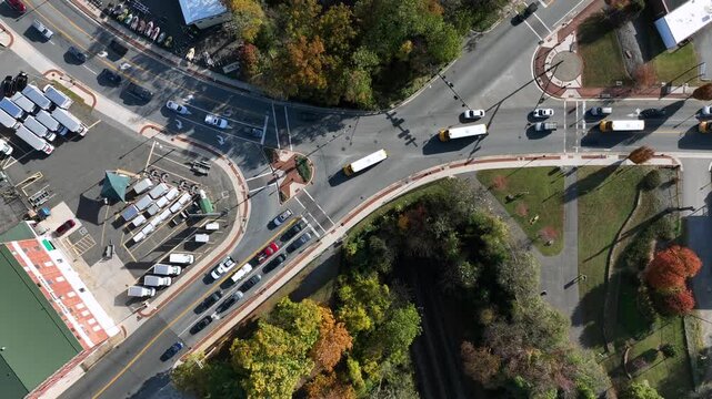Aerial top down of traffic scene on junction in American town. Sunny day in fall season with colored trees. Row of driving yellow school buses in autumn season.