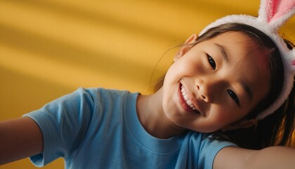 Portrait of little girl in blue t-shirt with Easter bunny ears on her head on a yellow isolated background. 
