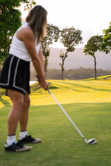 Hispanic woman golfer preparing for a golf swing on a green course during a beautiful sunset, enjoying an active luxury lifestyle
