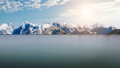 Frozen lake surface and majestic snow mountain peak under bright sun and blue sky