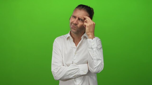 Blond man with long hair wearing white shirt touches temple with finger in studio with subtle puzzled expression; contemplation.