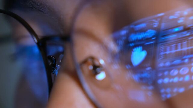 A person wearing glasses uses a laptop, with a real-time digital medical interface reflected in the lenses, representing healthcare analytics, clinical monitoring, and advanced medical technology.
