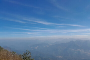 Peaceful layered mountain landscape under clear blue sky, soft clouds, calm atmosphere, natural light, realistic photography, high resolution.