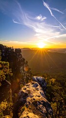 Scenic sun rising above rugged rocks, forests, and clouds