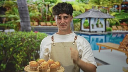 Man holding a tray of muffins clutches his head near a pool building, grimacing and clenching a fist; frustration mistake.