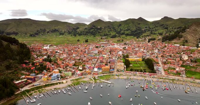 Cinematic aerial drone view of Copacabana town on the shore of Lake Titicaca. The harbor is filled with boats against a backdrop of green hills. Ideal for South American travel concepts, Bolivia