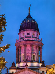 Illuminated French Cathedral at the Christmas market on Gendarmenmarkt in Berlin at blue hour, framed by Christmas tree lights and festive decorations in winter.