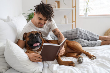 Young man with Boxer dog reading book in bedroom