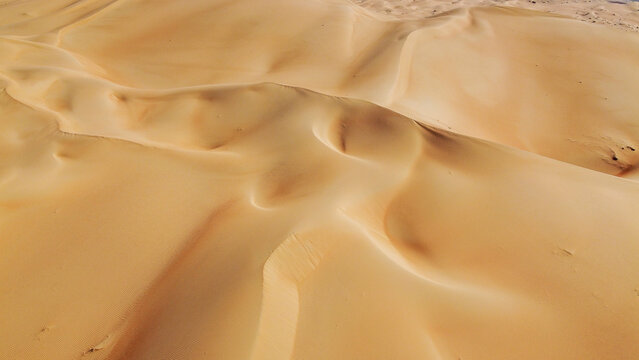 Expansive aerial perspective of rolling orange sand dunes in the Liwa Desert, Empty Quarter, UAE. Beautiful natural patterns and desert landscape under a clear sky