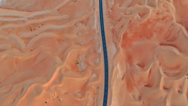 Dramatic bird's eye view of a black asphalt road winding through orange sand dunes in the Liwa Desert. Concepts of travel, isolation, and remote infrastructure