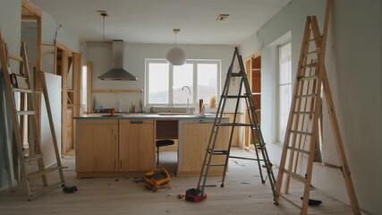 Renovation in progress, kitchen under construction with ladders and tools, viewed from the center of the room