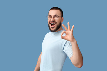 Fototapeta premium Young man in eyeglasses showing OK on blue background