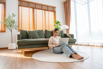 Young Asian beautiful woman relaxing on comfortable couch, using laptop at home, happy girl chatting with friends in social network, spending weekend, watching movie, shopping online