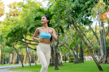 Asian woman jogging on a pathway in a public park, wearing athletic clothing and enjoying a cardio workout in a green, natural environment