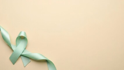 Soft mint green satin ribbon tied in a awareness loop against a textured beige background