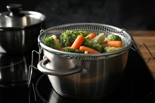 Mixed vegetables steaming in metal colander over pot on stove