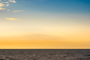 Obraz premium Nature sky breathtaking golden sunset over a calm ocean, with the entire sky and water bathed in brilliant shades of yellow and orange. Streaky clouds enhance the dramatic display of light 