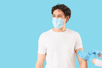 Young man in medical mask receiving vaccine from doctor's hands on blue background. Immunity concept