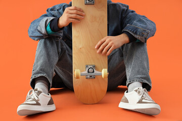 Young man with skateboard sitting on orange background, closeup © Pixel-Shot