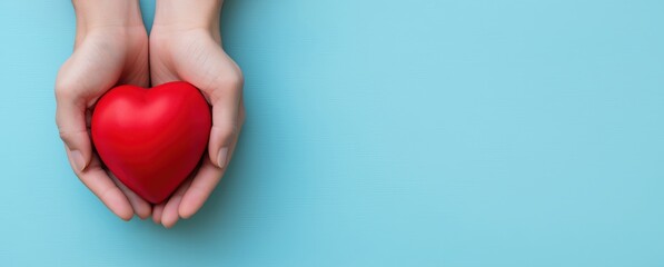 Hands holding a red heart, symbolizing love, health, donation, and care on a blue background with copy space