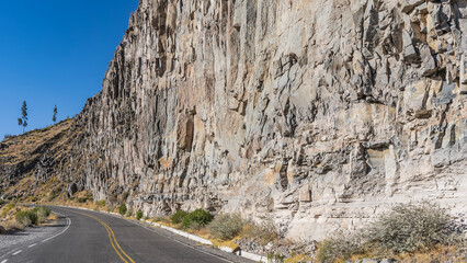 The road runs along a sheer cliff. The highway turns. A yellow dividing line on the asphalt. The blue sky. Peru