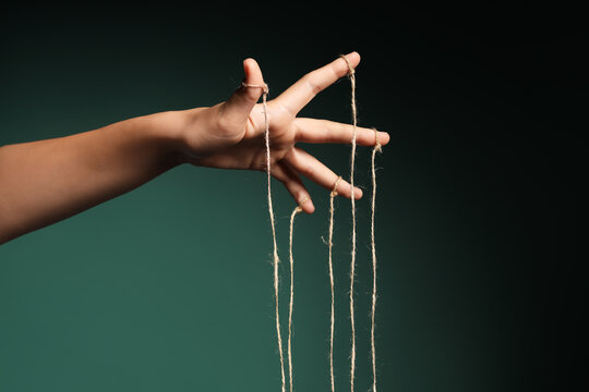 Female hand of puppeteer with strings on dark green background