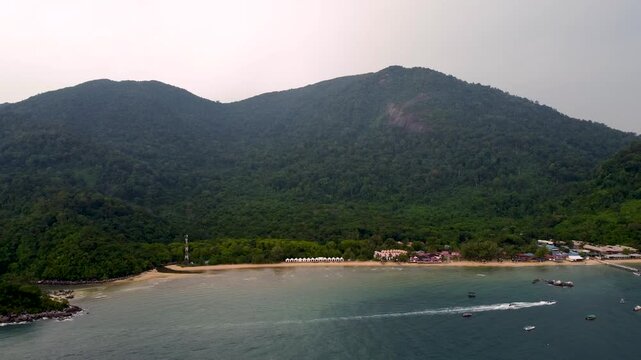 Aerial drone flyaway from a tropical island, revealing boats crossing blue ocean water as the island becomes smaller in the distance. Ideal for travel, tourism, freedom, and exploration.