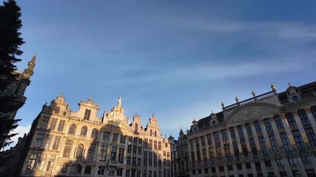 Slow motion left-to-right pan across guildhall buildings on Grand Place, lit by winter sunset with Christmas setup visible.