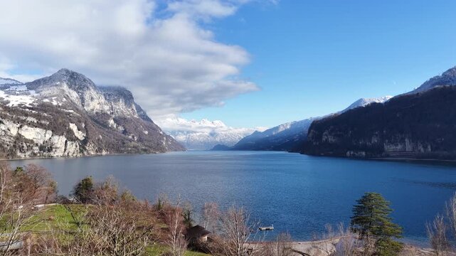 Drone pushes toward wide blue lake surrounded by alpine mountains and winter peaks at Walensee, Switzerland, natural landscape and outdoor scenery.
