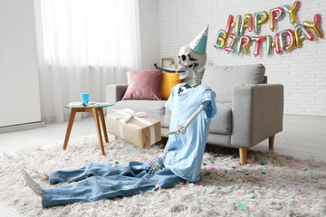 Skeleton in clothes with party hat, whistle and gift in living room decorated for birthday