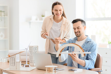 Male architect and his assistant working with 3D model of bridge at table in office