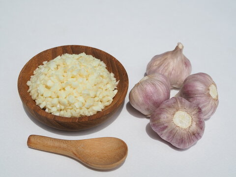 Chopped garlic is placed in a wooden bowl on a white background.