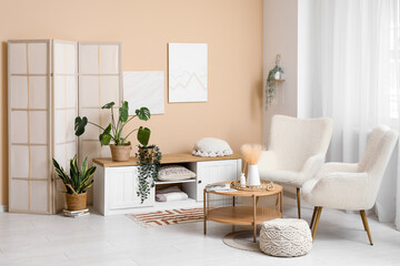 Fototapeta premium Interior of modern room with folding screen and houseplants near beige wall