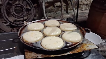 Traditional Indonesian apem cake being cooked on a hot pan, showing the step-by-step street food baking process with soft batter rising into golden, fluffy cakes