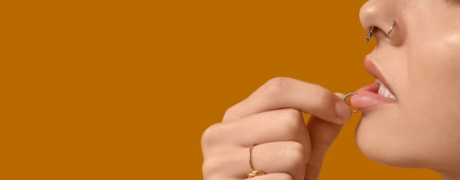 Young woman with nose and lip piercing on yellow background with space for text, closeup