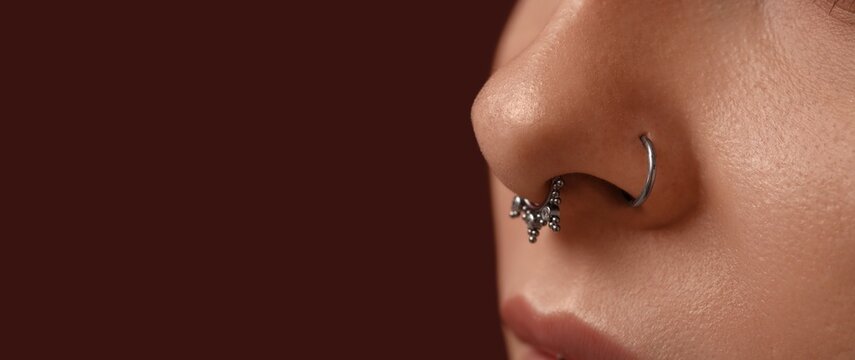 Young woman with nose piercing on dark background with space for text, closeup