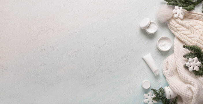 Cosmetic products with Christmas decorations and warm winter clothes on blue background