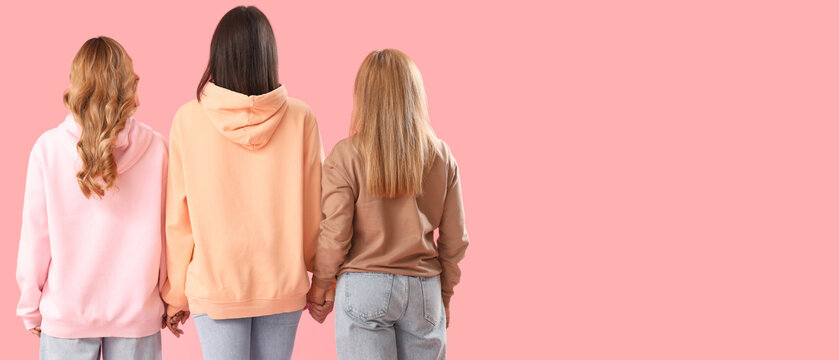 Women holding hands on pink background, back view