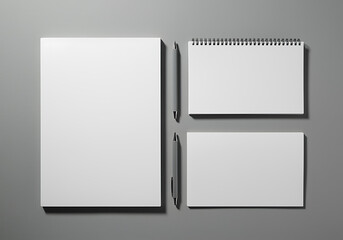 A spiral bound notebook and two notepads with pens on a gray surface for office or school supplies