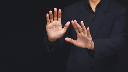 Business person showing stop gesture with both hands on dark background.